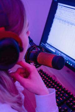 Woman blogger using condenser microphone during online podcast in room with neon light