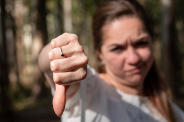 Mujer rechazando con el gesto de pulgar abajo, mostrando su puño a cámara. Fotografía con enfoque selectivo en la mano - obrazy, fototapety, plakaty