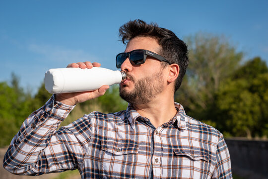 Hombre apuesto tomando l&iacute;quido de botella met&aacute;lica en blanco, para anuncios o propagandas. Fotograf&iacute;a con enfoque selectivo en la botella
