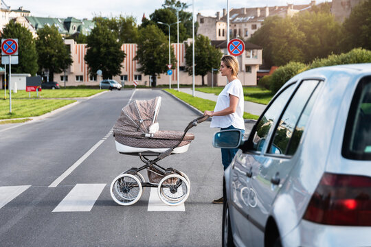 Young mother with the baby pram is walking by the crosswalk