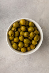 White bowl full of juicy green olives on a light background