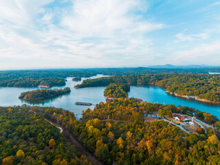 Fototapeta premium Lake Lanier in North Georgia, aerial drone on a sunny fall day. Radiant clouds both blue and white. Clear view of fall colored trees and blue lake water.