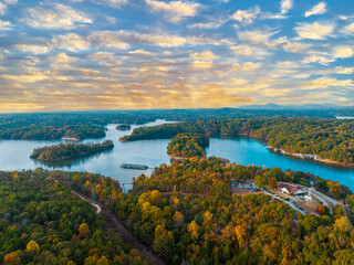 Lake Lanier in North Georgia, 4K aerial drone on a sunny fall day. Radiant clouds both blue and orange. Clear view of fall colored trees and blue lake water. - Powered by Adobe