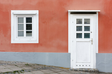 Detail of the facade of a building with the wall painted in orange and a door and a window in white