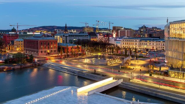 Dawn in Oslo Norway: night to day time-lapse of the city center, featuring water canal and white bridge as well as lights in illuminated downtown square - skyline and cityscape.