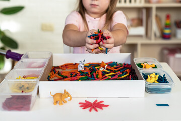 Little girl toddler playing with sensory bin with colored dyed pasta. Sensory play and learning colors activity for kids, material Montessori, games for fine motor skills, craft activities