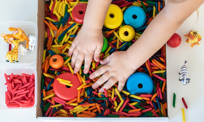 Child hands playing with dyed pasta for sensory play and craft activities. Learning colors activity for kids, activities Montessori, games for fine motor skills, play for toddler.