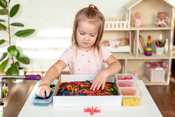 Little girl toddler playing with sensory bin with colored dyed pasta. Sensory play and learning...