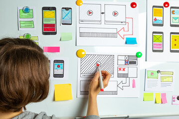 Website developer. A woman designer is working on sketches of mobile applications for smartphones....