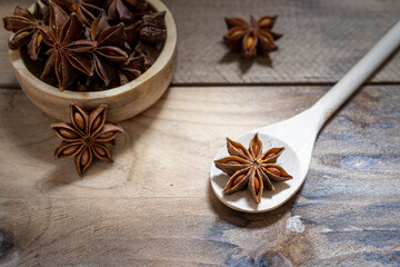 Anise stars (Illicium verum ) in wooden spoon and wooden bowl on dark rustic wooden background.