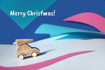 Wooden toy, silhouette of Christmas tree on toy car on colored layered paper background. Xmas...