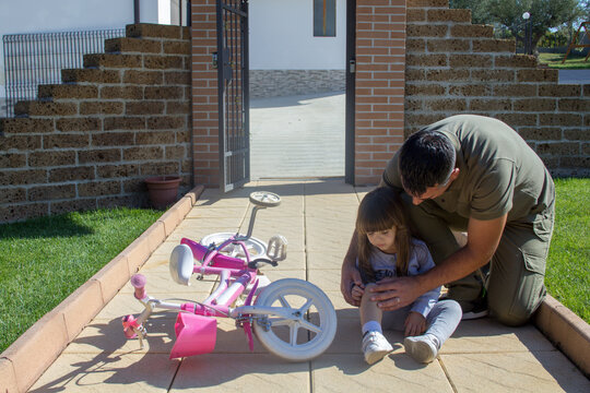Image of a young dad helping his daughter who fell on her bike and has a skinned knee. Little girl looking for help after falling with her bicycle
