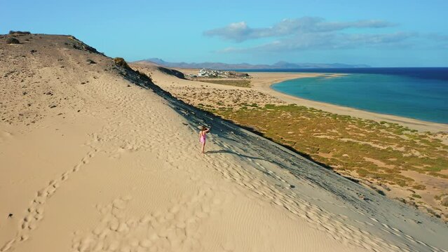 Playa Esmeralda. Jandia, Spain beach. Sunrise over cityscape. Aerial flight. Sand golden dunes, desert hills. Arid dry hiking area. Woman enjoys vacation. Time to travel. Fuerteventura Island.