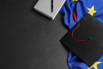 Graduation cap, book, pen and flag of European Union on black table, flat lay. Space for text