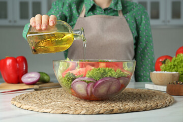Woman pouring oil from glass bottle into bowl with salad in kitchen, closeup