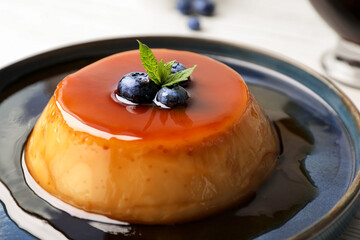 Plate of delicious caramel pudding with blueberries and mint on table, closeup