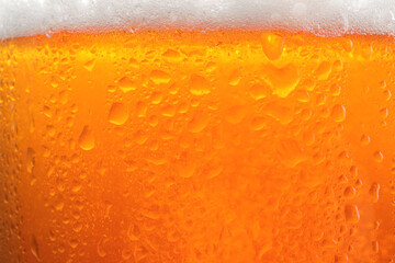 Glass of tasty cold beer with foam and condensation drops as background, closeup