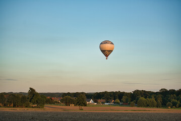 Hot air balloon rides over fields, forests and houses in the evening sun