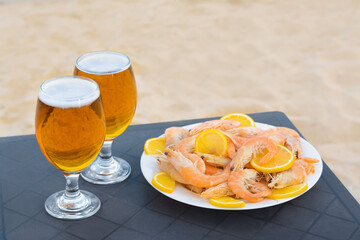 Cold beer in glasses and shrimps served with lemon on beach