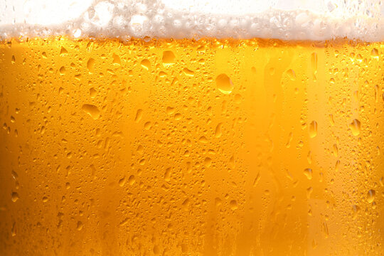 Glass of tasty cold beer with foam and condensation drops on white background, closeup