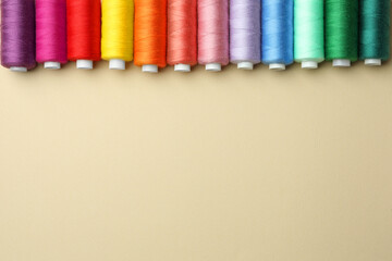 Set of colorful sewing threads on beige background, flat lay. Space for text