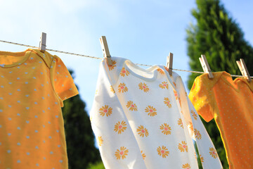 Clean baby onesies hanging on washing line in garden. Drying clothes