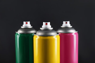 Colorful cans of spray paints on black background, closeup