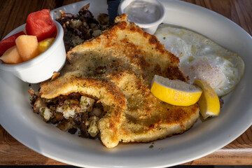 Seafood breakfast consisting of calamari steak, fried eggs, fruit and potato on white plate in a restaurant setting viewed from dinner angle - 543551038