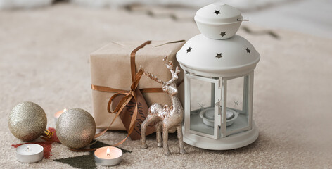 Christmas lantern with burning candles, gift and decor on floor in room