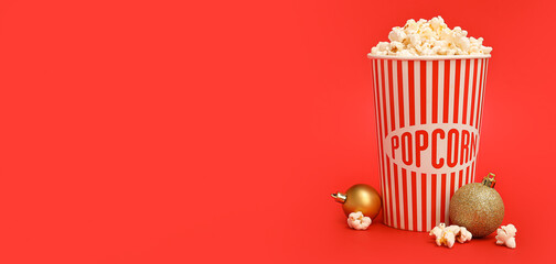 Bucket of popcorn with Christmas balls on red background with space for text