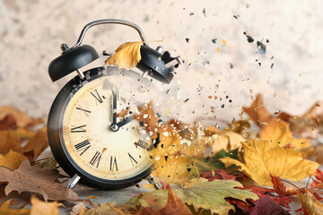 Crumbling alarm clock with autumn leaves on grunge background