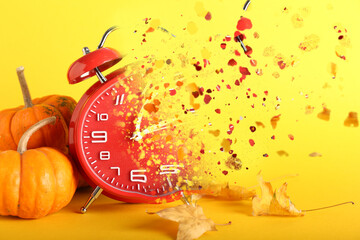 Crumbling alarm clock with autumn leaves and pumpkins on yellow background