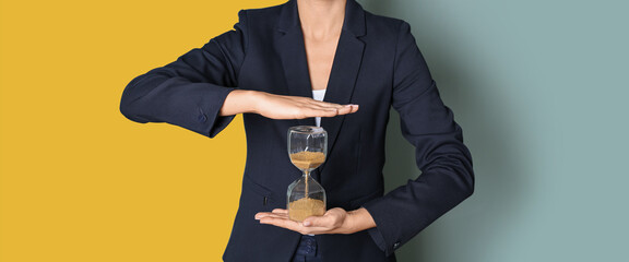 Businesswoman holding hourglass on color background. Time management concept