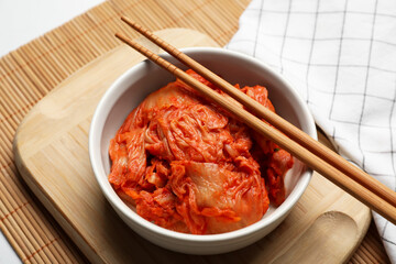 Bowl of spicy cabbage kimchi with chopsticks on bamboo mat