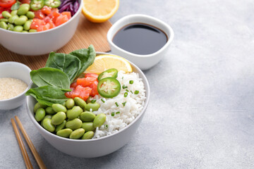 Poke bowl with salmon, edamame beans and rice on light grey table, space for text
