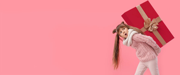 Cute little girl carrying big Christmas gift on pink background with space for text