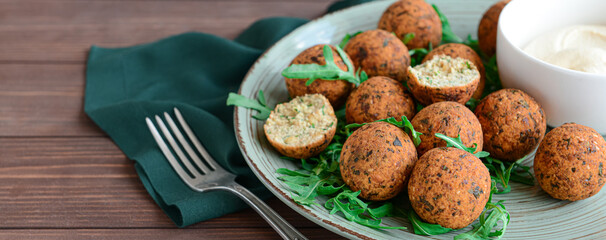 Plate with tasty falafel balls and sauce on wooden table, closeup