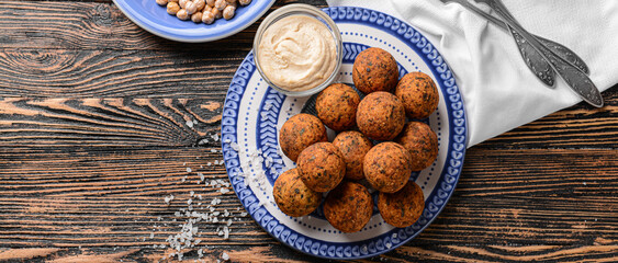 Plate with tasty falafel balls and sauce on wooden table, top view