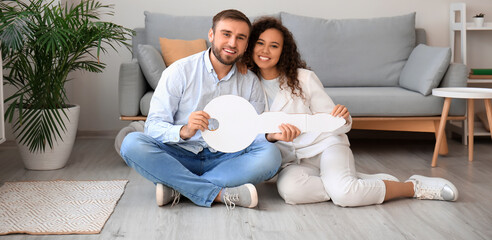 Happy young couple with big paper key in new flat