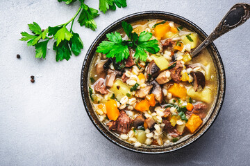 Autumn food. Warming soup with pumpkin, mushrooms, vegetables, beef and barley. Gray table background, top view
