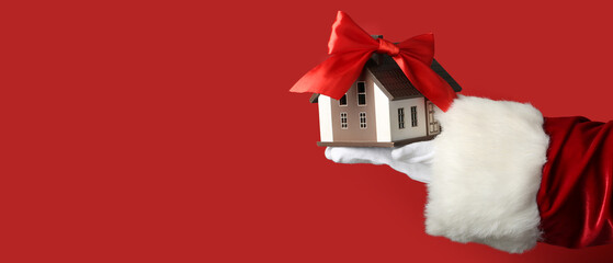 Santa Claus holding model of house with ribbon bow on red background with space for text. Concept...