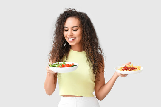 Happy Young African-American Woman With Healthy And Unhealthy Food On Light Background. Diet Concept