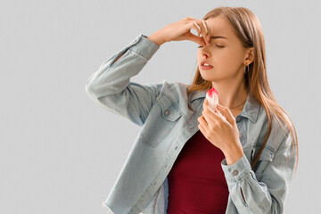 Young woman with nosebleed and tissue on light background