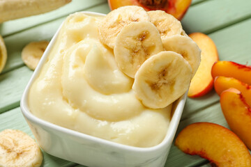 Bowl of tasty vanilla pudding with banana on color wooden table, closeup