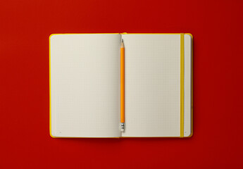 Notebook and pencil on red background, top view
