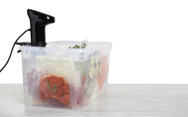 Sous vide cooker and vacuum packed food products in box on wooden table against white background,...