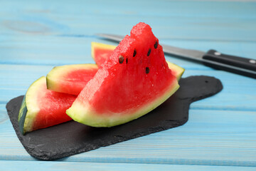 Slate board with slices of juicy watermelon on light blue wooden table