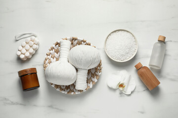 Flat lay composition with herbal massage bags and other spa products on white marble table