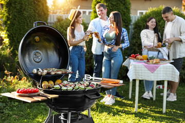 Group of friends having party outdoors. Focus on barbecue grill with food