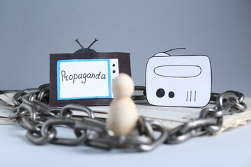 Propaganda concept. Human mired in media field. Chained wooden figure, newspapers, paper TV and...